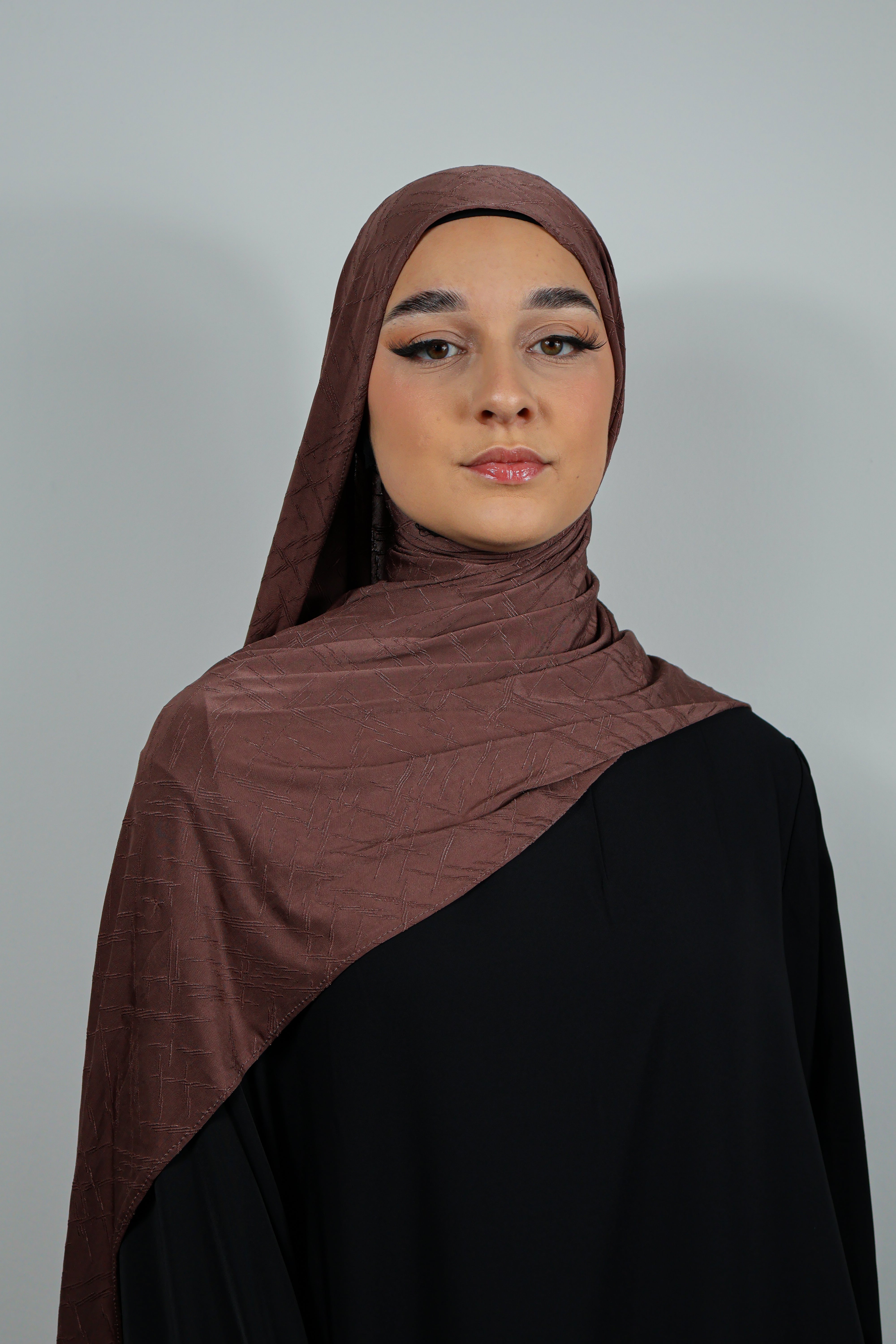 Femme portant un hijab en Jersey Prestige noir texturé, élégamment drapé sur une abaya noire.
